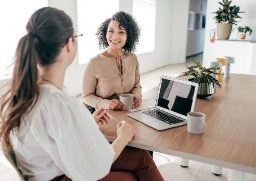 Two people talking at a table in front of an open laptop